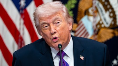 Donald Trump speaks into a microphone while sitting at a table