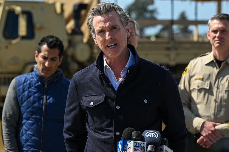 California Governor Gavin Newsom speaks during a press conference outdoors as two other men stand behind him.