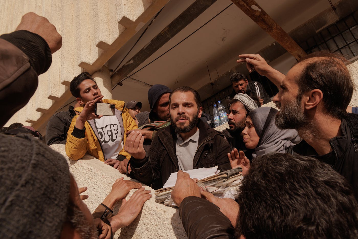 A man, who had collected folders full of personal information from Sednaya prison, addresses the crowd, attempting to organize the chaotic process of locating their loved ones held in Sednaya Prison.