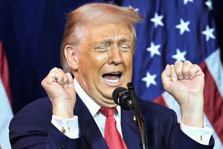 Donald Trump holds up his fists while speaking into a microphone