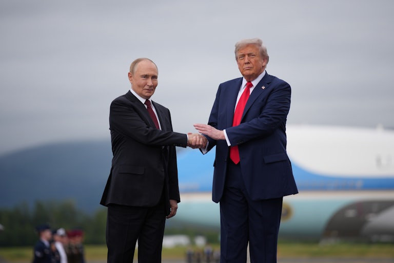 Russian President Vladimir Putin and Donald Trump shake hands while standing on the tarmac of a military base in Alaska
