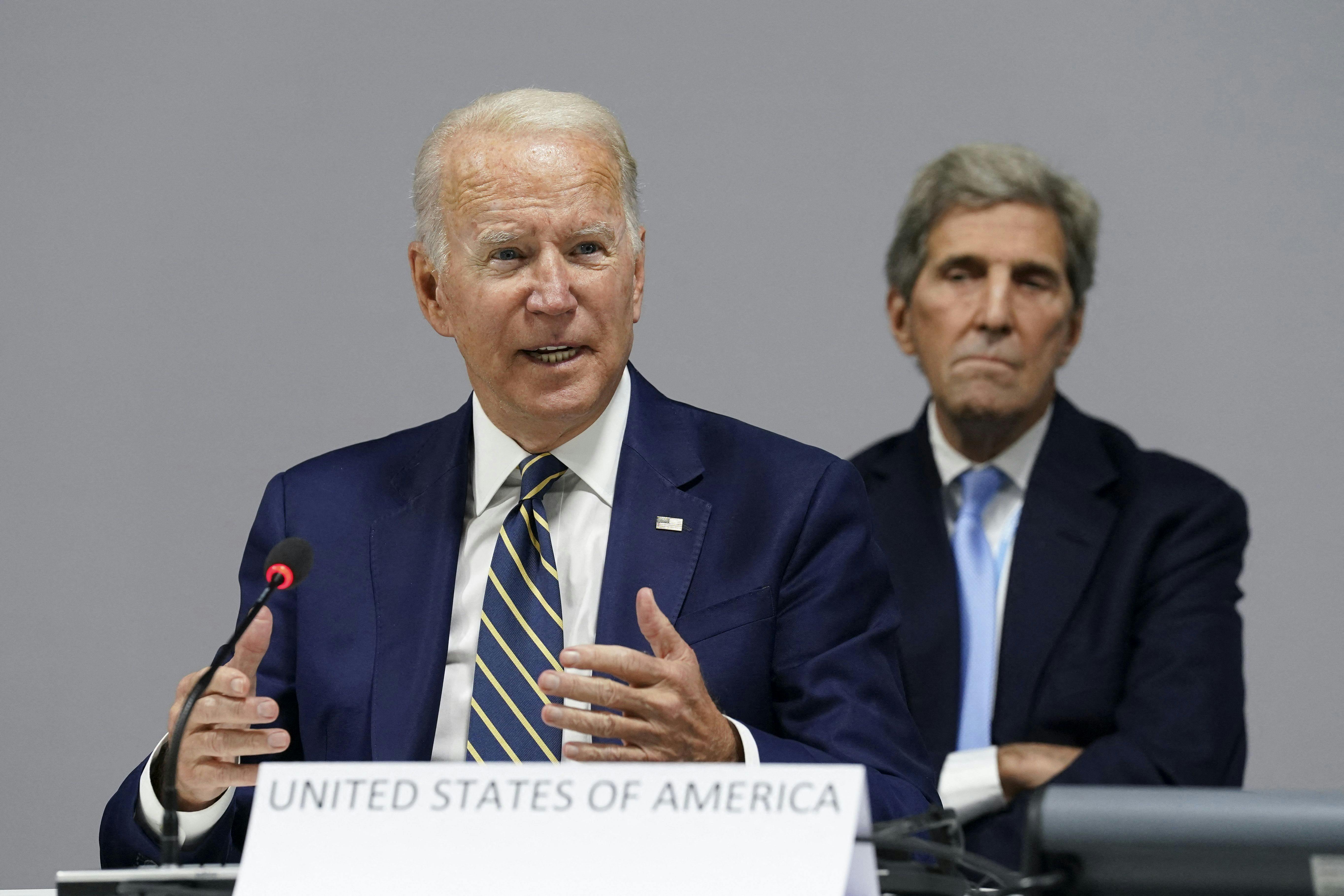 Joe Biden speaks at COP26, with John Kerry in the background.