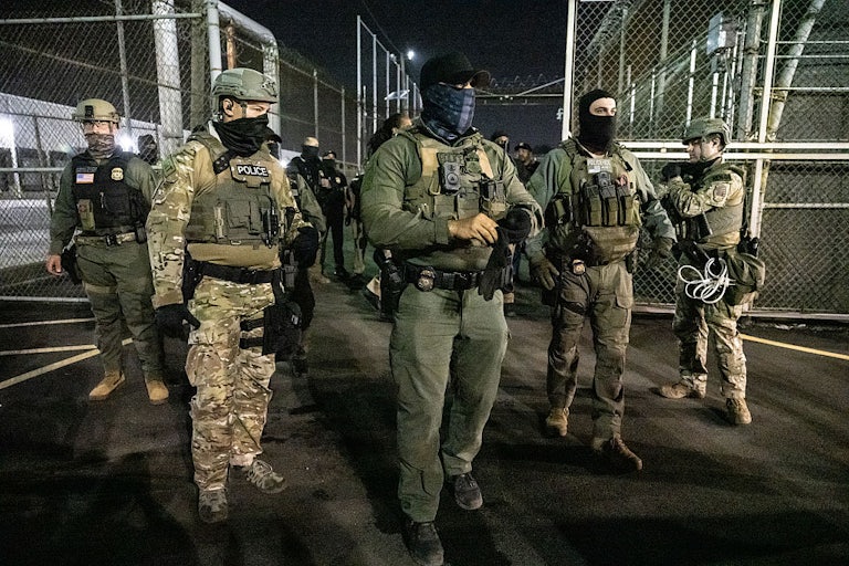 ICE agents wearing masks, police vests, and camoflauge stand outside Delaney Hall in the night.