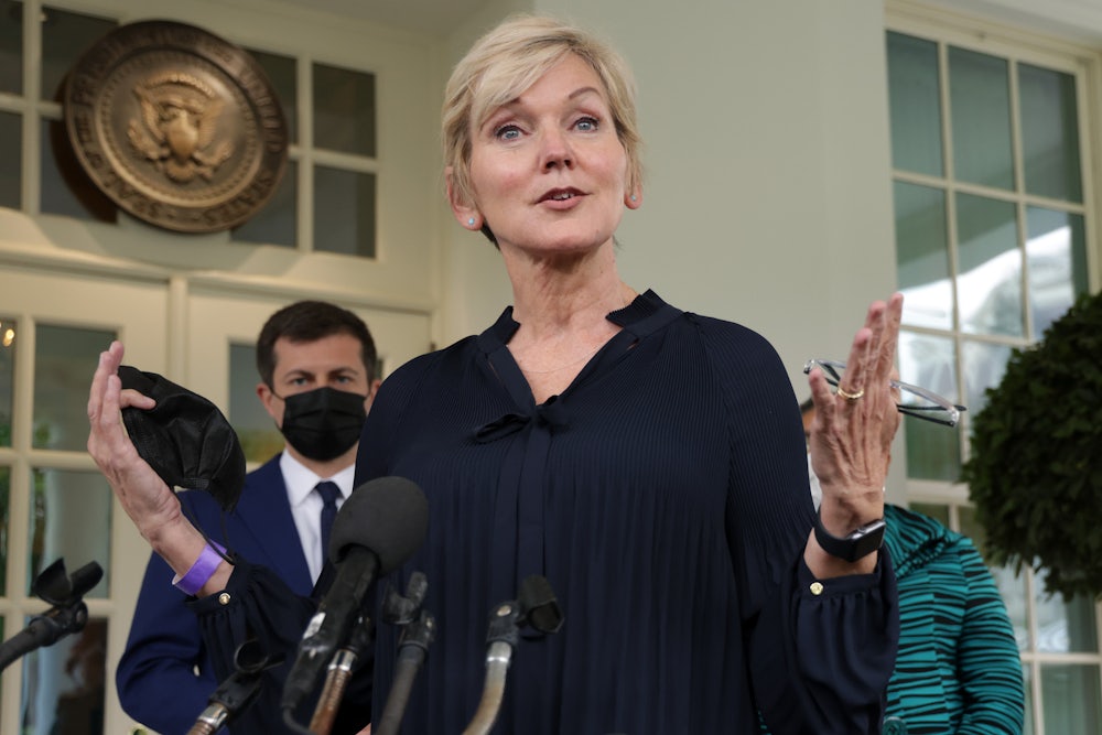 Jennifer Granholm speaks in front of microphones, with Pete Buttigieg in the background.