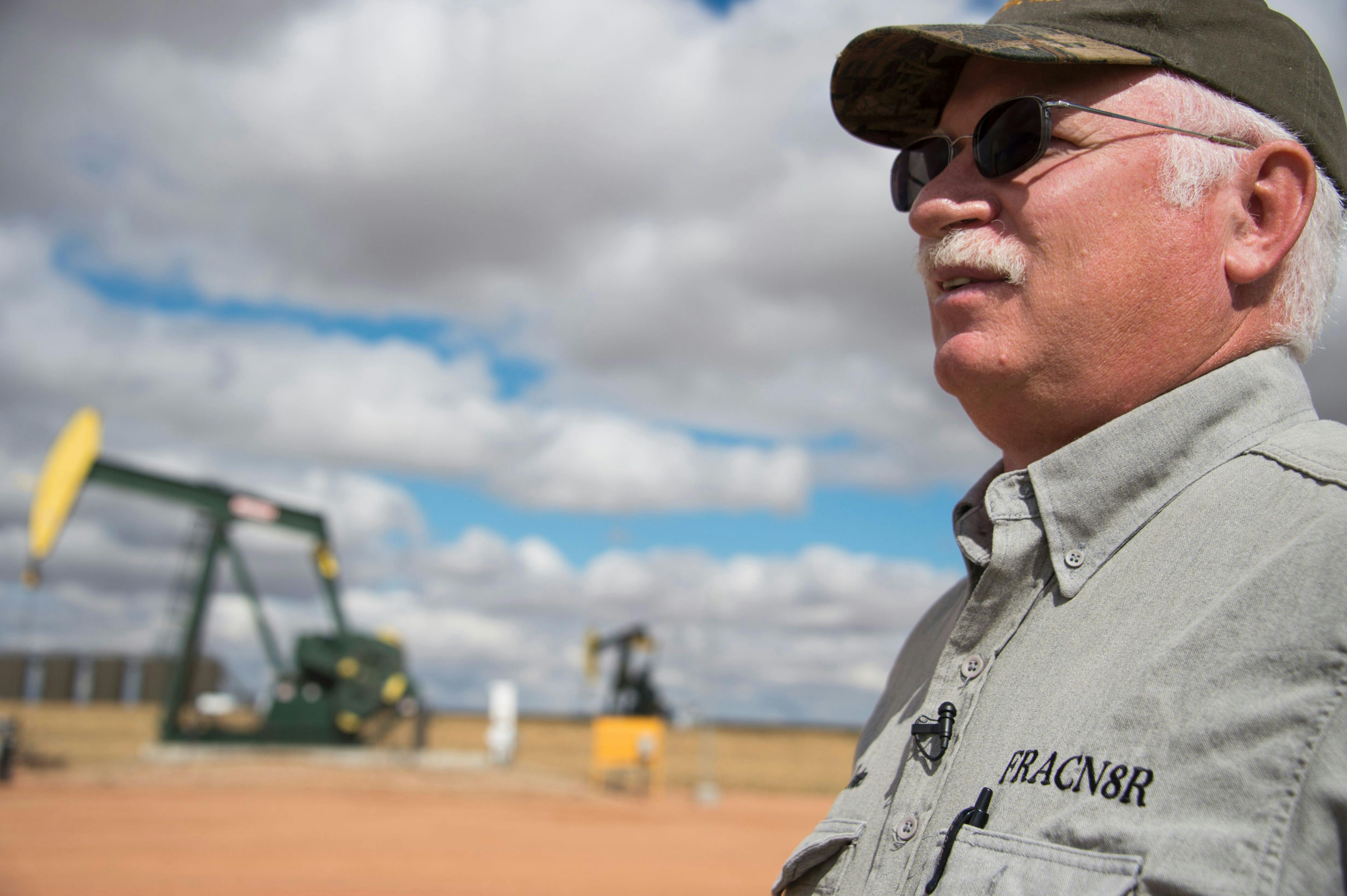 An oil industry consultant talks in front of a drilling rig.