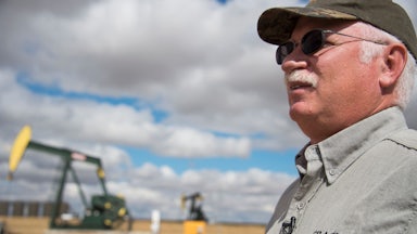 An oil industry consultant talks in front of a drilling rig.