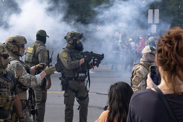 Tear gas fills the air as federal immigration agents point their guns at people.