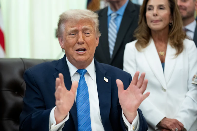 Donald Trump gestures with both hands and speaks while sitting at his desk in the Oval Office
