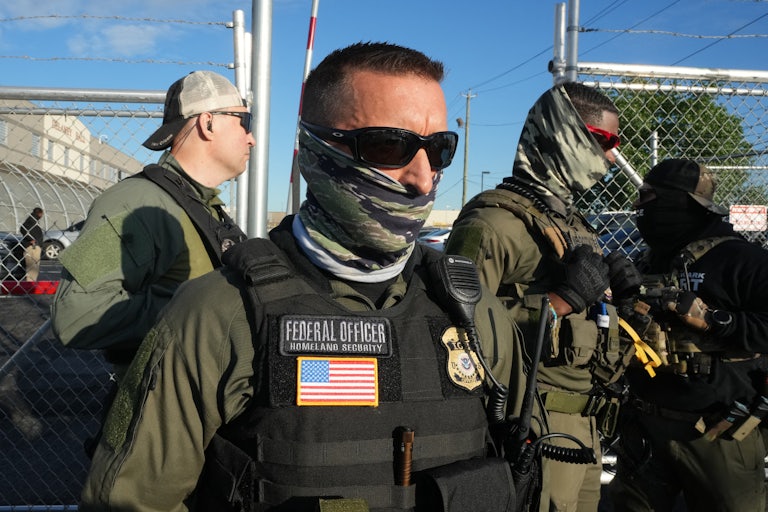 Immigration and Customs Enforcement (ICE) agents stand near a gate at an immigrant detention center.