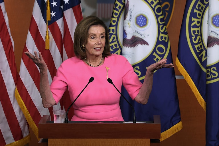 Nancy Pelosi stands behind a lectern shrugging at a press conference on Capitol Hill.