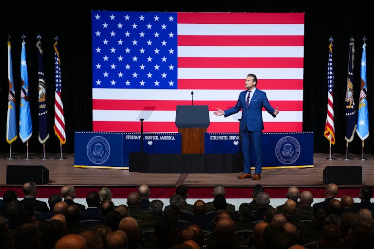 War Secretary Pete Hegseth holds his arms out to the side while speaking to military leaders at Quantico military base