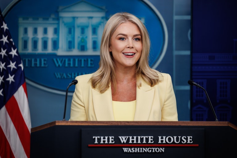 Karoline Leavitt smiles at the podium in the White House Press Briefing Room.