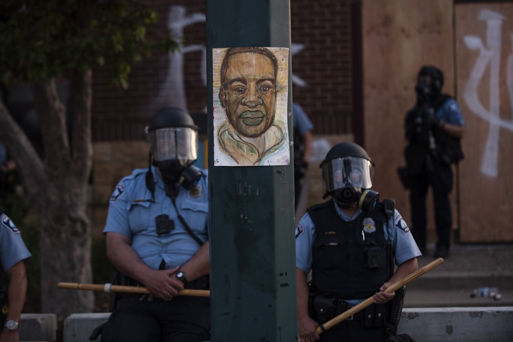 On May 27, 2020, a portrait of George Floyd hung on a street light between two officers policing a protest in Minneapolis's Third Precinct.