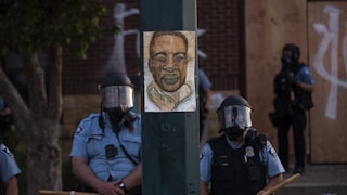On May 27, 2020, a portrait of George Floyd hung on a street light between two officers policing a protest in Minneapolis's Third Precinct.
