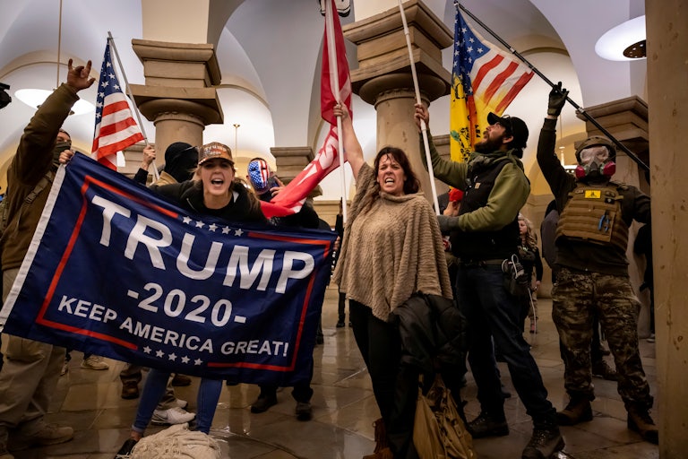 Trump supporters inside the Capitol hold U.S. flags and a Trump 2020 banner. The woman holding the Trump banner yells at the camera.