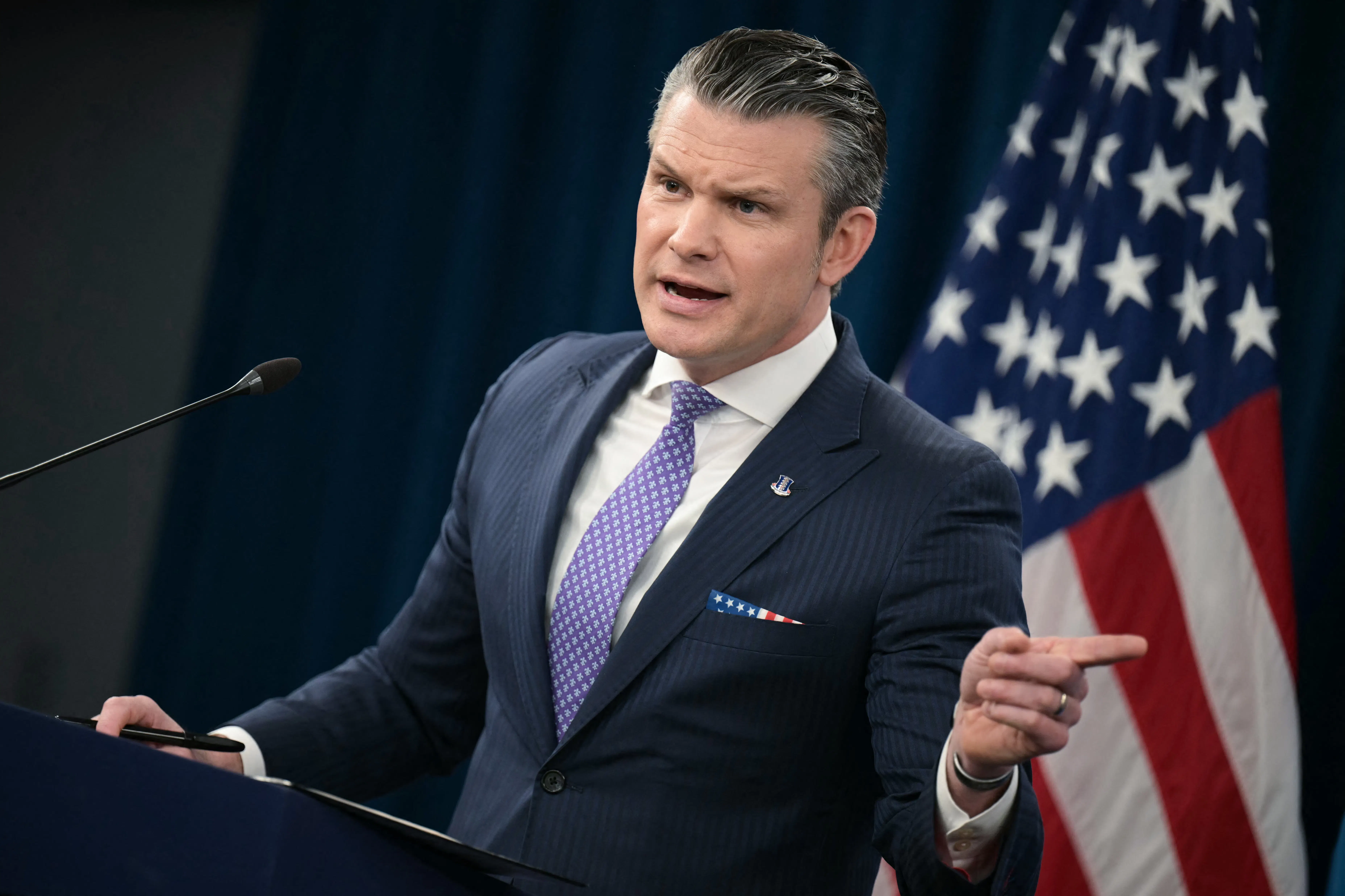 Defense Secretary Pete Hegseth points to the side while speaking at a podium