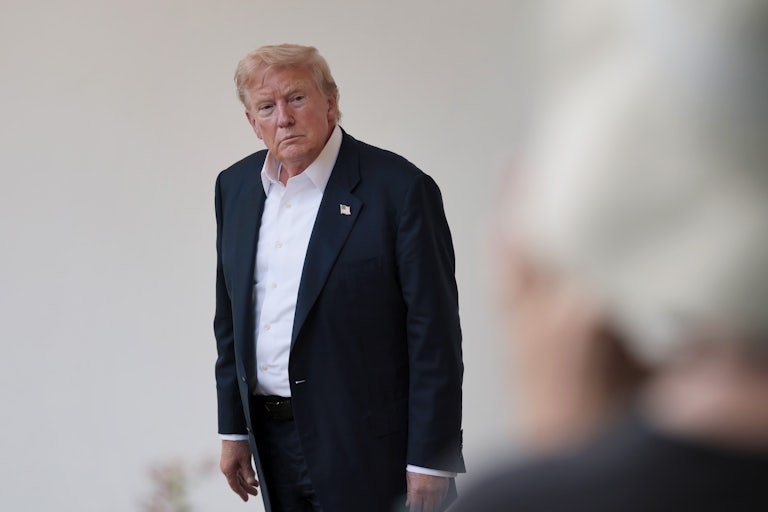 Donald Trump leaning forward slightly with hunched shoulders.