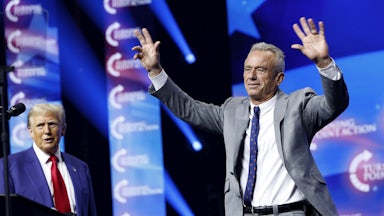 Robert F. Kennedy Jr. walks forward with his hands raised, as Trump stands to the side.