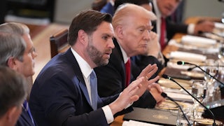 JD Vance puts both hands up while speaking, seated at a long table with Donald Trump on his left