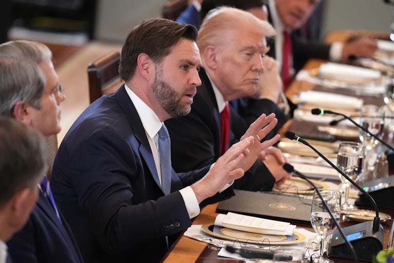 JD Vance puts both hands up while speaking, seated at a long table with Donald Trump on his left