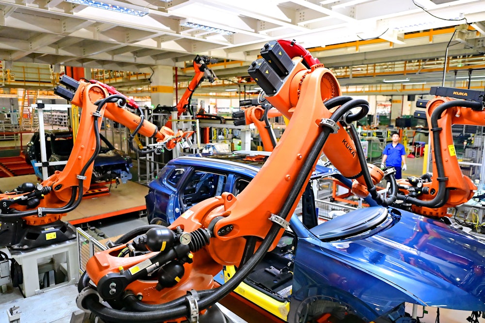 Several robotic arms extend over the frame of a vehicle, with a person in the background looking on.