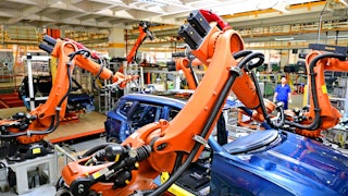 Several robotic arms extend over the frame of a vehicle, with a person in the background looking on.