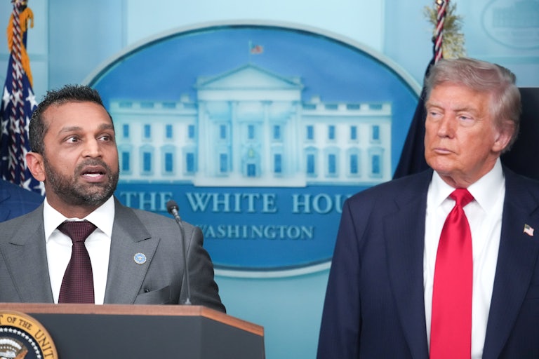 FBI Director Kash Patel speaks at the podium in the White House press briefing room while Donald Trump stands next to him
