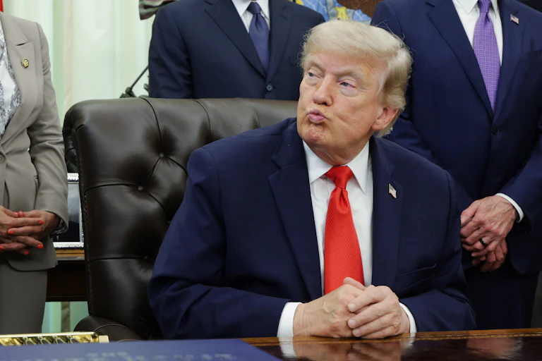 Donald Trump puckers his lips while sitting with his hands folded on his desk in the Oval Office