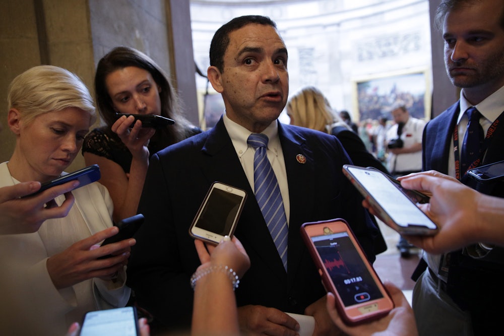 Henry Cuellar stands surrounded by members of the media, who are extending phones towards him.