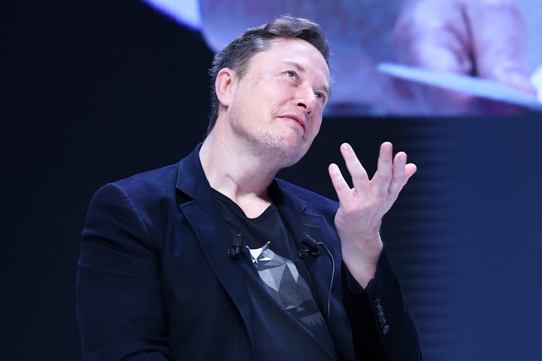 Elon Musk smiles smugly and makes a hand gesture as if in question