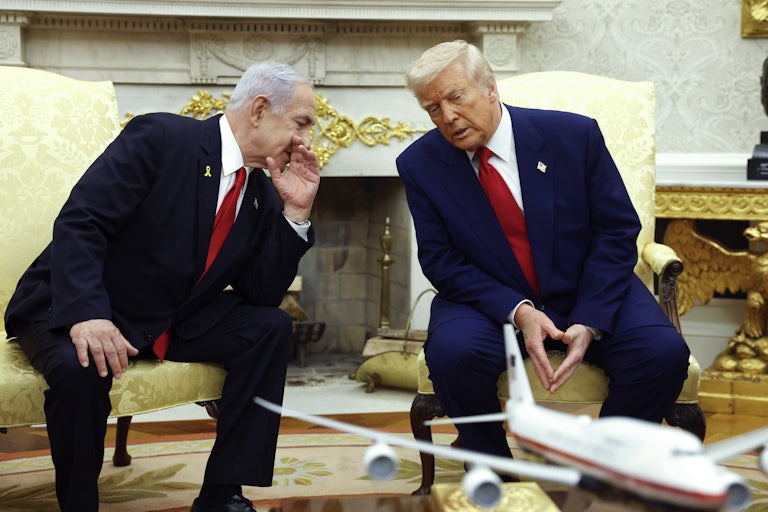 Benjamin Netanyahu leans over and covers his mouth as he says something to Donald Trump, as he leans in to listen. Both sit in the Oval Office of the White House.