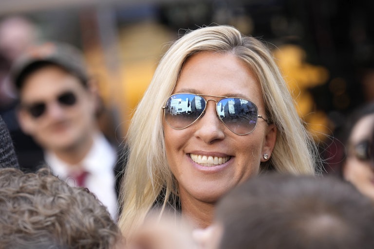 Marjorie Taylor Greene, wearing aviator sunglasses, flashes a toothy smile.
