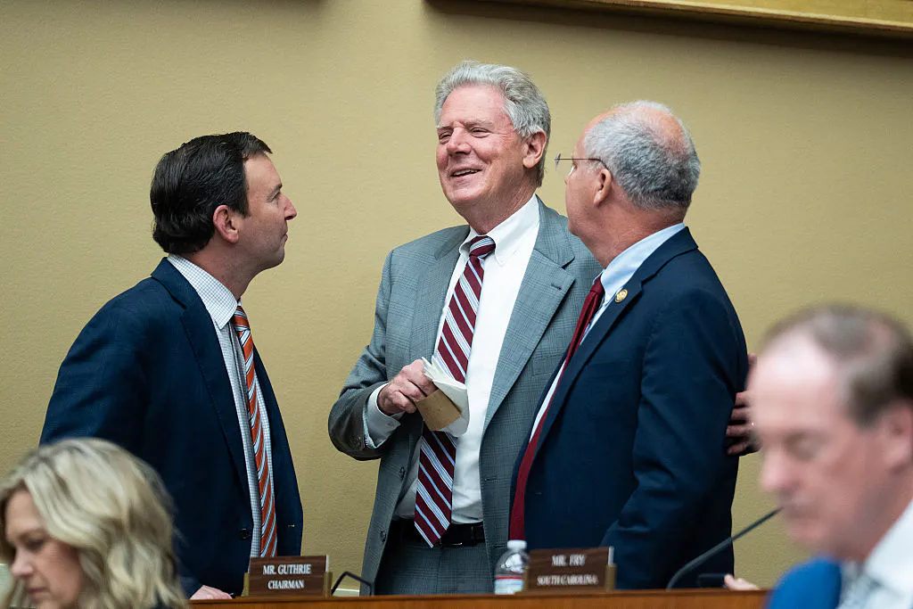 Frank Pallone Jr., Craig Goldman, and Brett Guthrie talk in a huddle while standing, with others' heads visible in the foreground.