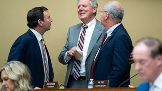 Frank Pallone Jr., Craig Goldman, and Brett Guthrie talk in a huddle while standing, with others' heads visible in the foreground.