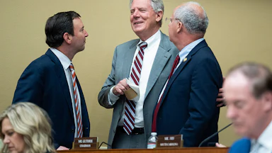 Frank Pallone Jr., Craig Goldman, and Brett Guthrie talk in a huddle while standing, with others' heads visible in the foreground.
