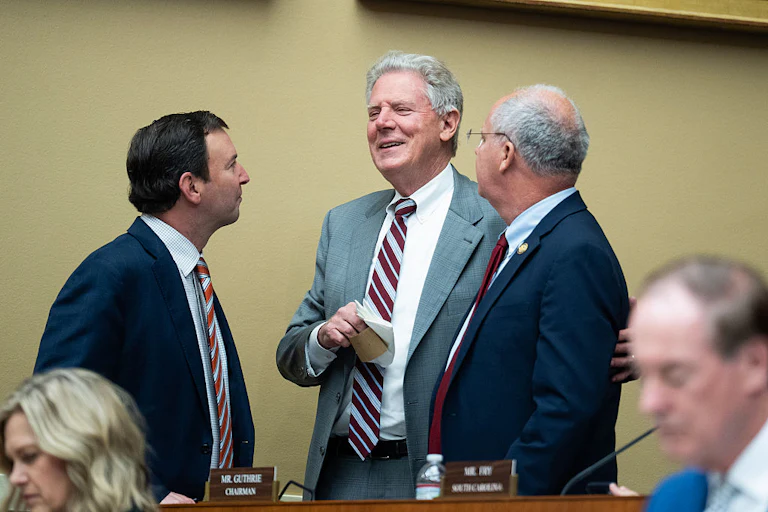 Frank Pallone Jr., Craig Goldman, and Brett Guthrie talk in a huddle while standing, with others' heads visible in the foreground.