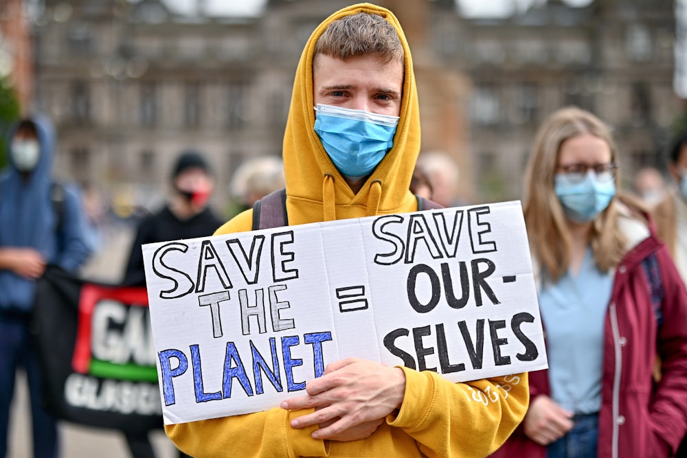 A young man in a hoodie holds a sign reading "save the planet = save ourselves."