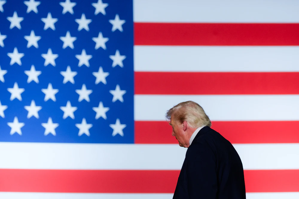 Trump is seen in profile against a large background of an American flag.