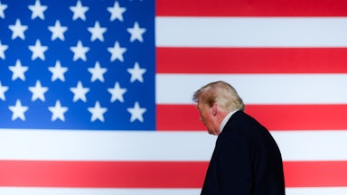 Trump is seen in profile against a large background of an American flag.