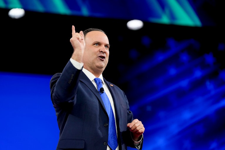 Dan Scavino talks on a stage and points his finger in the sky.