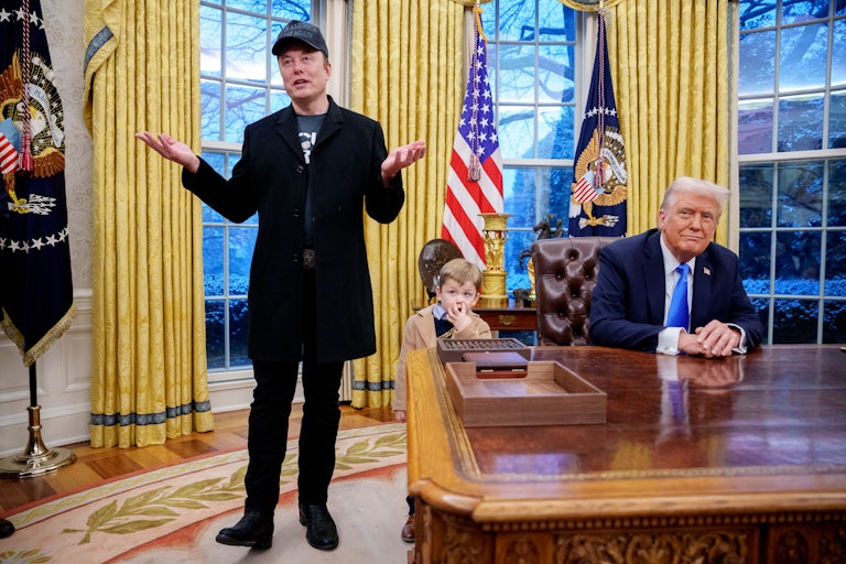 Elon Musk stands in the Oval Office of the White House and raises his arms as if to shrug. His young son X stands near Donald Trump as he sits behind his desk.