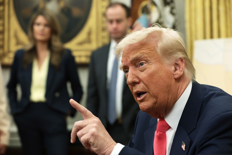 Donald Trump speaks and points a finger while seated at his desk in the Oval Office.