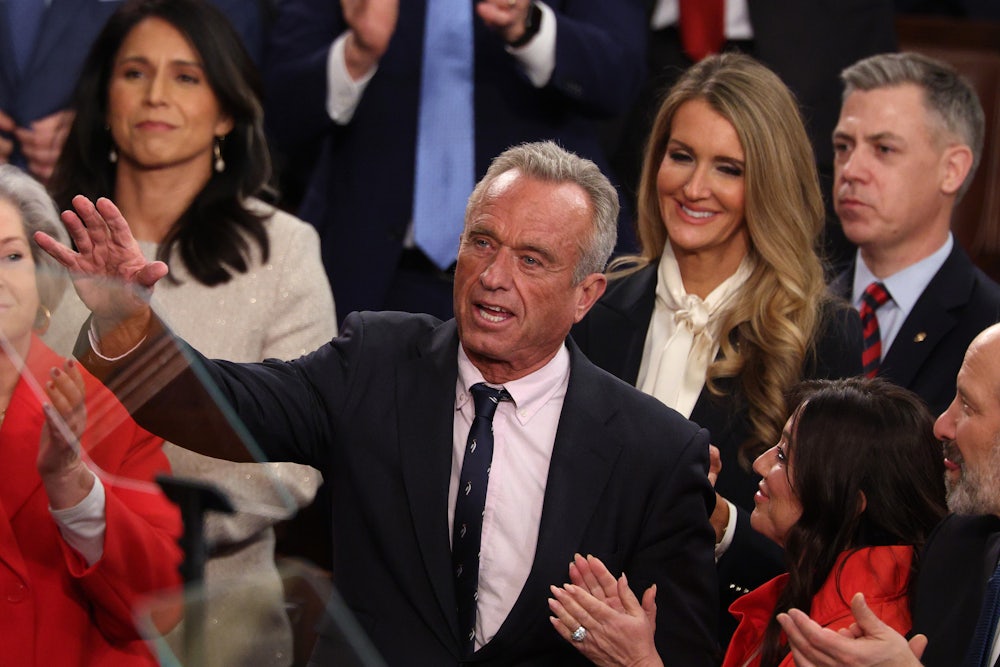 RFK Jr. smiles while raising a hand as people around him smile and clap.