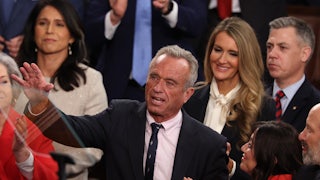 RFK Jr. smiles while raising a hand as people around him smile and clap.
