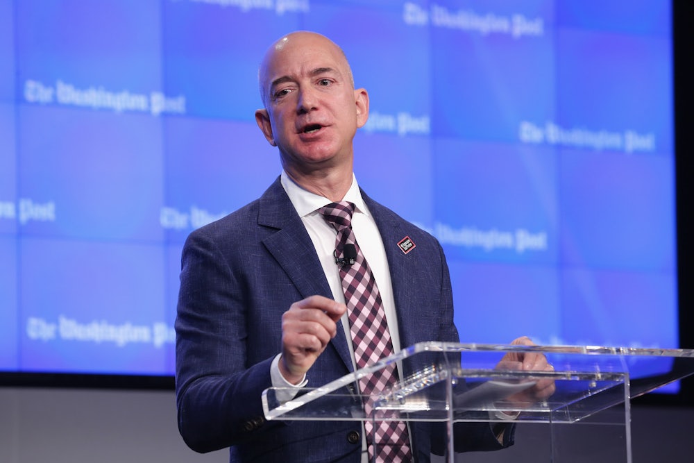 Jeff Bezos stands at a podium in front of a screen marked "The Washington Post."