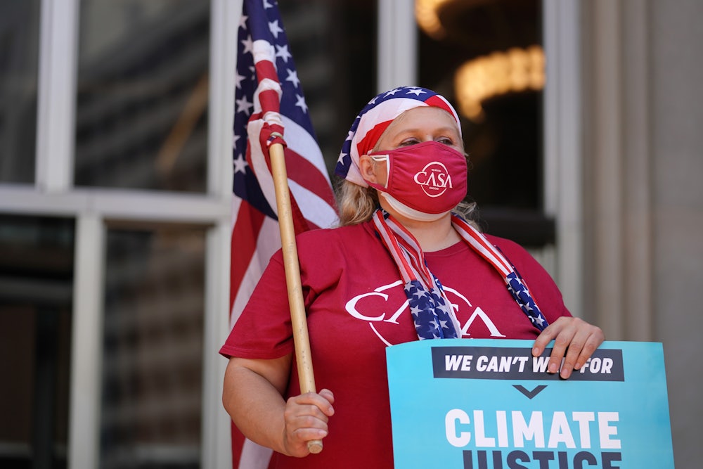 A demonstrator draped in American flag iconography holds a "climate justice" sign.