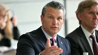 Defense Secretary Pete Hegseth gestures and speaks while sitting at a conference table