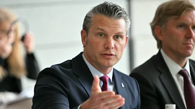 Defense Secretary Pete Hegseth gestures and speaks while sitting at a conference table