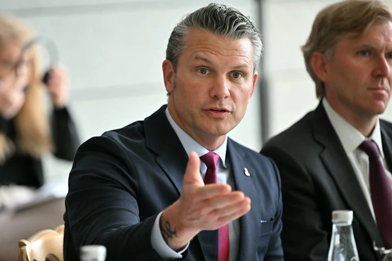 Defense Secretary Pete Hegseth gestures and speaks while sitting at a conference table