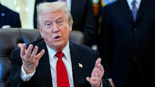 Donald Trump speaks with both hands while sitting behind his desk in the Oval Office of the White House. (He seems like he's pleading, or confused.)